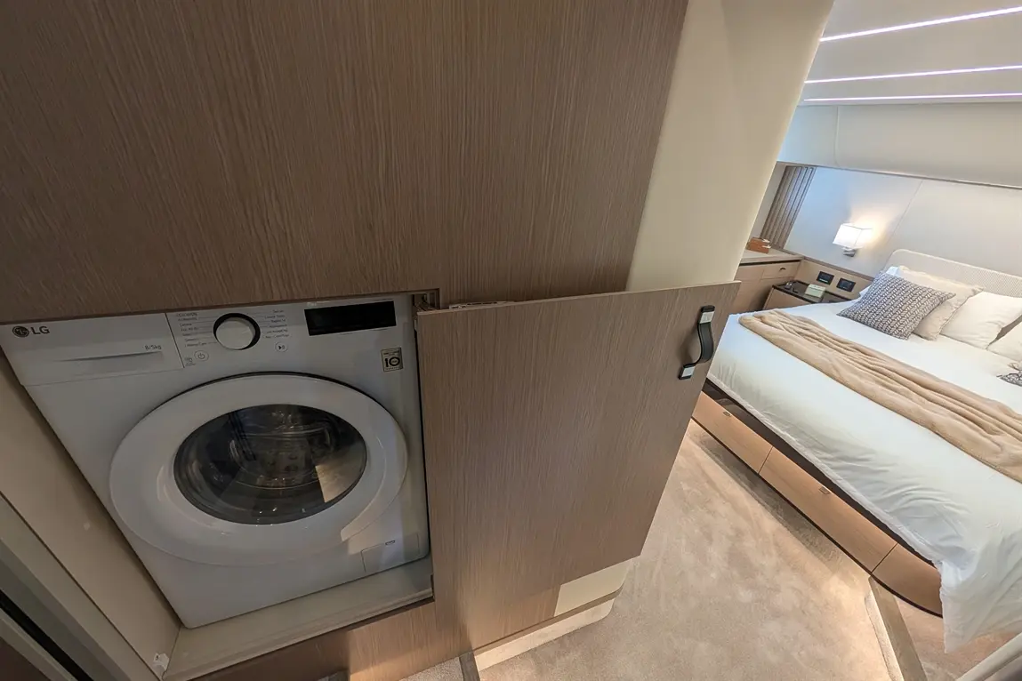 A modern bedroom featuring a hidden LG washing machine in cabinetry, with a bed adorned with plush pillows and a soft throw.
